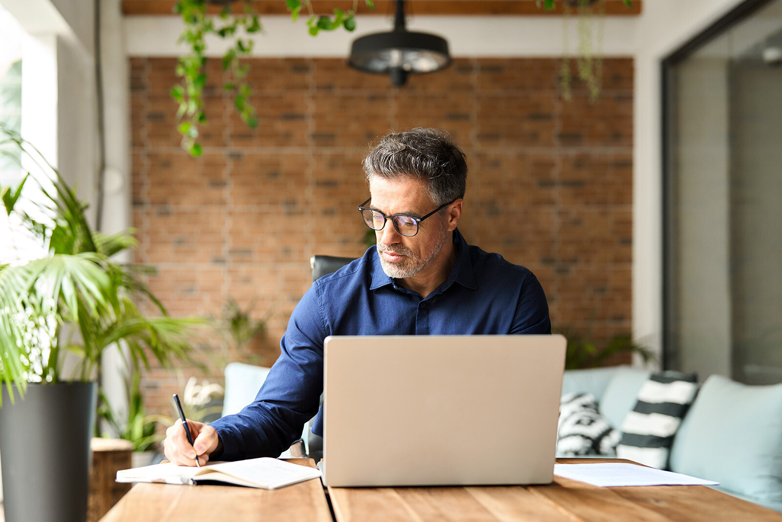 man in an office working on a laptop and writing down notes